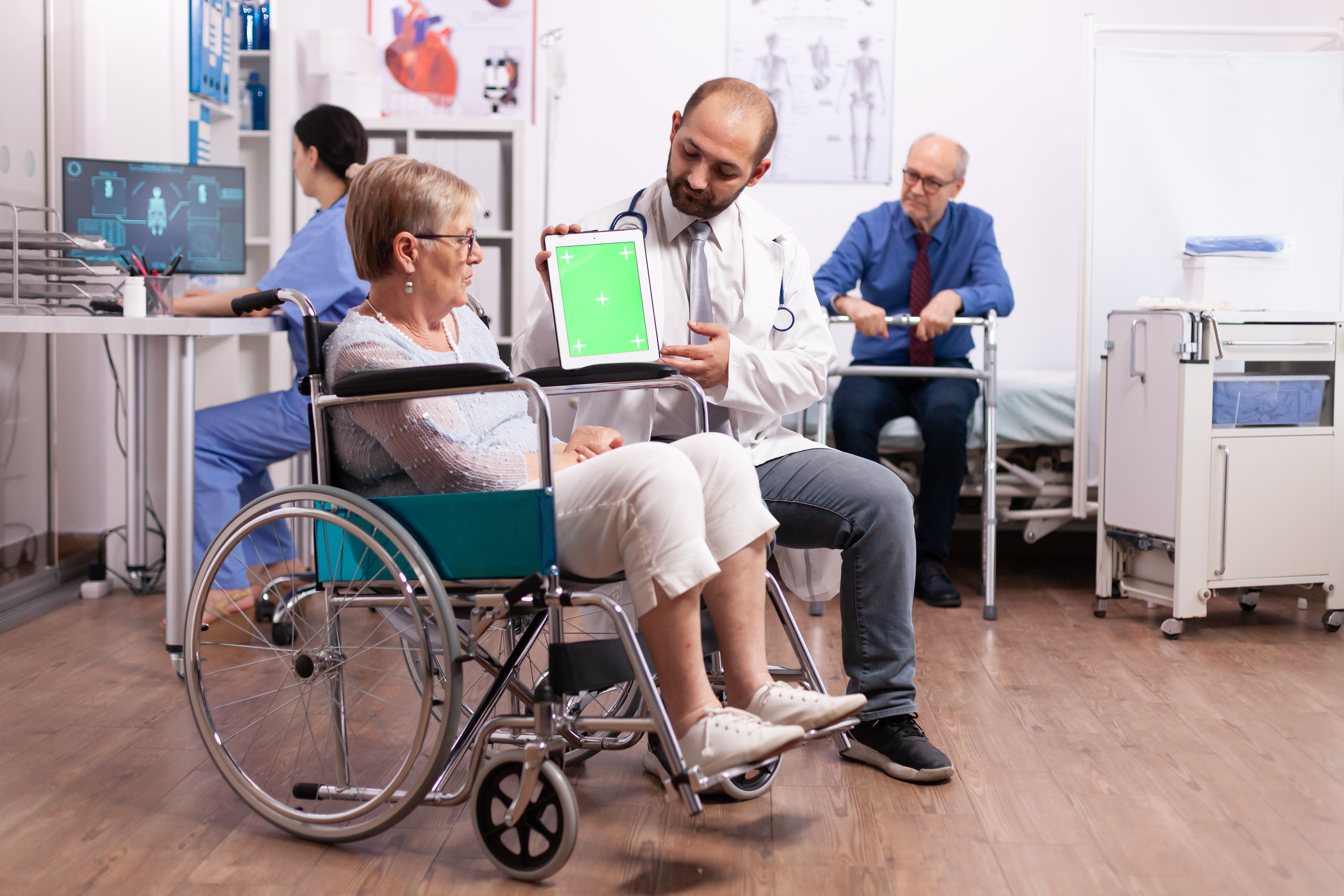 Hospital staff consulting handicapped senior woman sitting in wheelchair holding tablet pc with green screen. Medical practitioner using device with chroma key during coonsultation of invalid senior woman.
